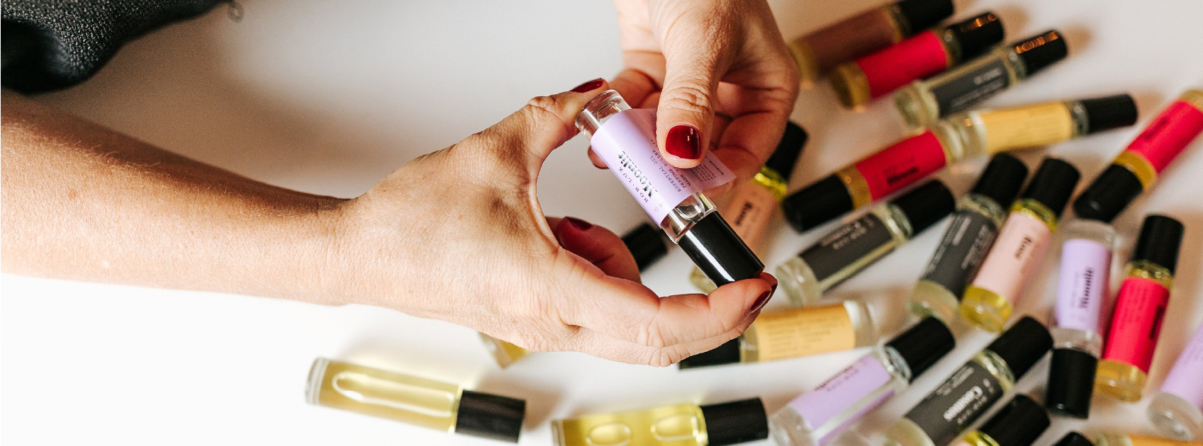 pair of hands holding essential oil by bon lux on top of bottles of other bon lux products